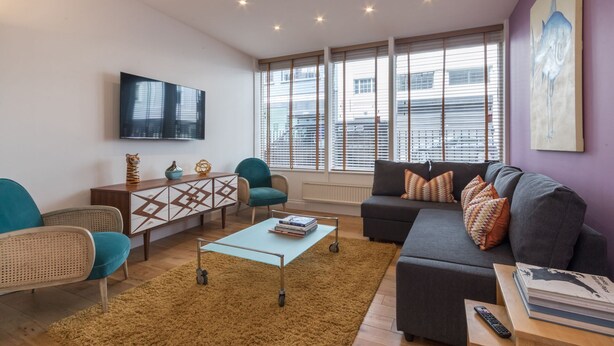 A modern living room with a sofa, chairs, a coffee table, and a TV. - Fitzrovia Duplex · 2-Bed · Private Patio Garden (London)