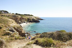 A coastal landscape with a rocky beach, clear blue sea, and a few people walking on a dirt path. - 200 m from the beach, lovely flat for 4 people (Saint-Gildas-de-Rhuys)