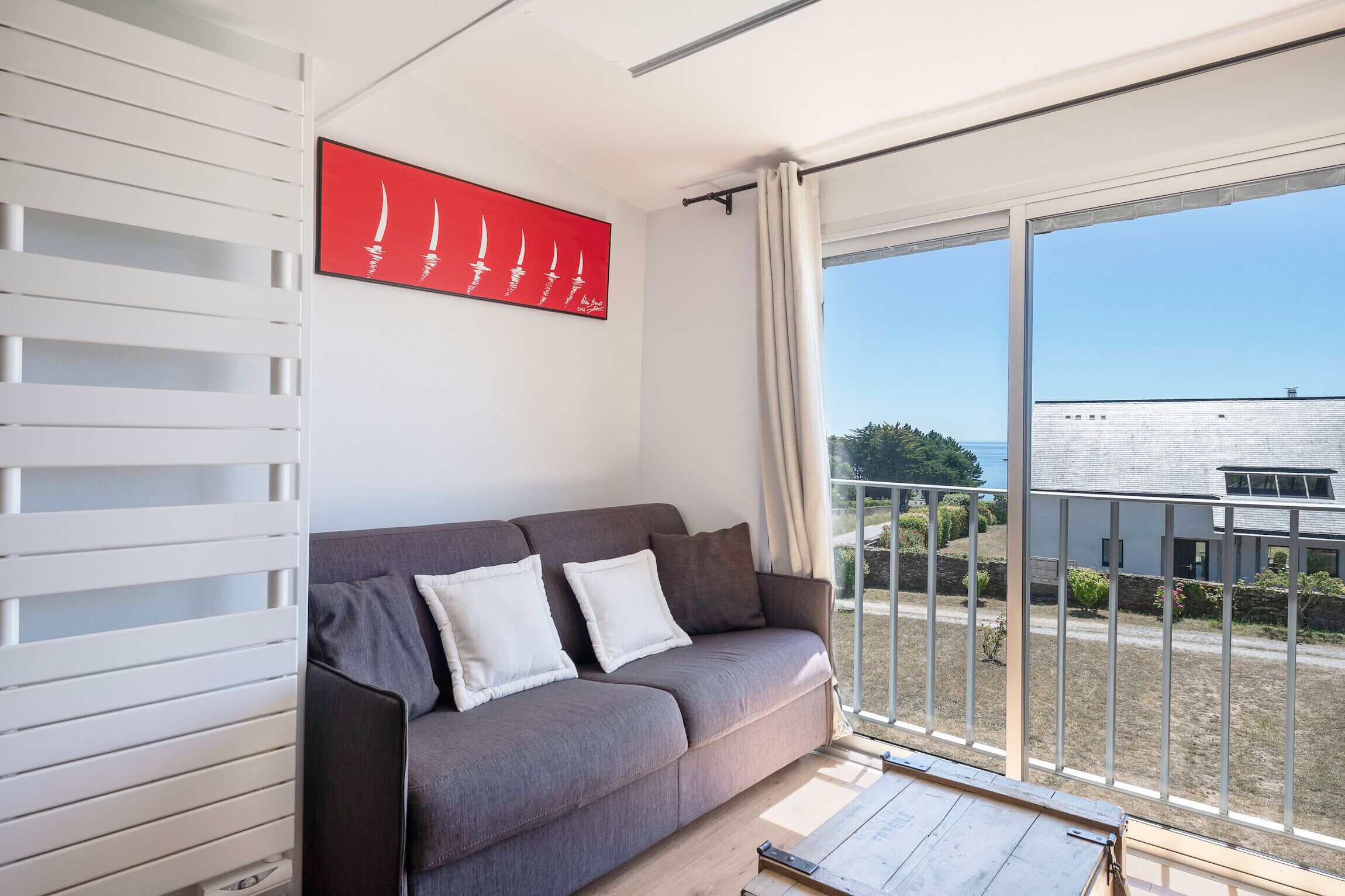 Una sala de estar moderna con un sofá gris, una obra de arte roja y un amplio ventanal corredero a un balcón.