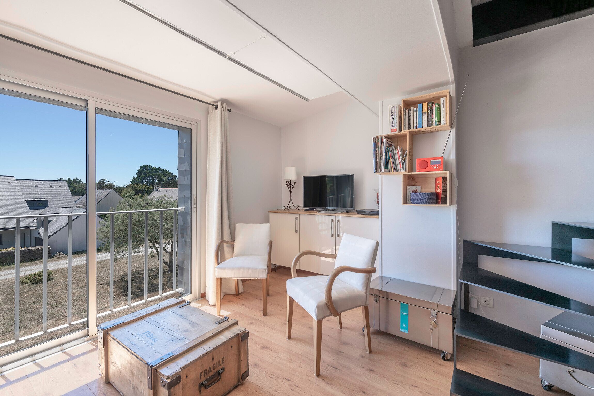 Un soggiorno moderno con un'ampia porta-finestra in vetro, una TV a schermo piatto, un mobiletto in legno e una libreria.