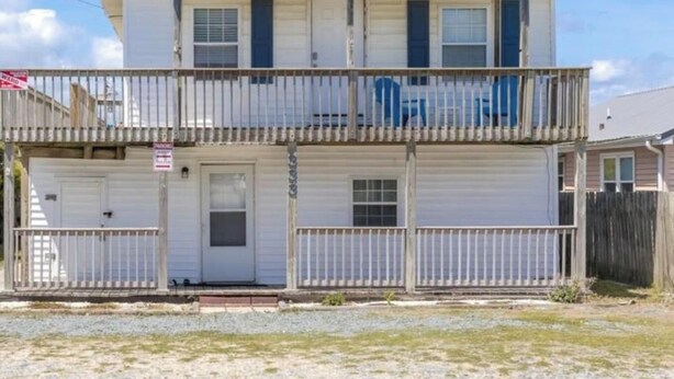 A two-story building with a balcony, a garage door, and a small front yard. - The Treasure Chest - 3 BR/2 BA Upper Part of Duplex in the Heart of Surf City (Surf City)