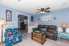 A living room with a sofa, a floral armchair, a vintage trunk, and a ceiling fan. - The Treasure Chest - 3 BR/2 BA Upper Part of Duplex in the Heart of Surf City (Surf City)