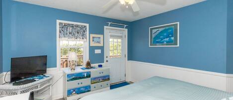 A bedroom with a bed, a desk with a computer, a ceiling fan, and a window with curtains.