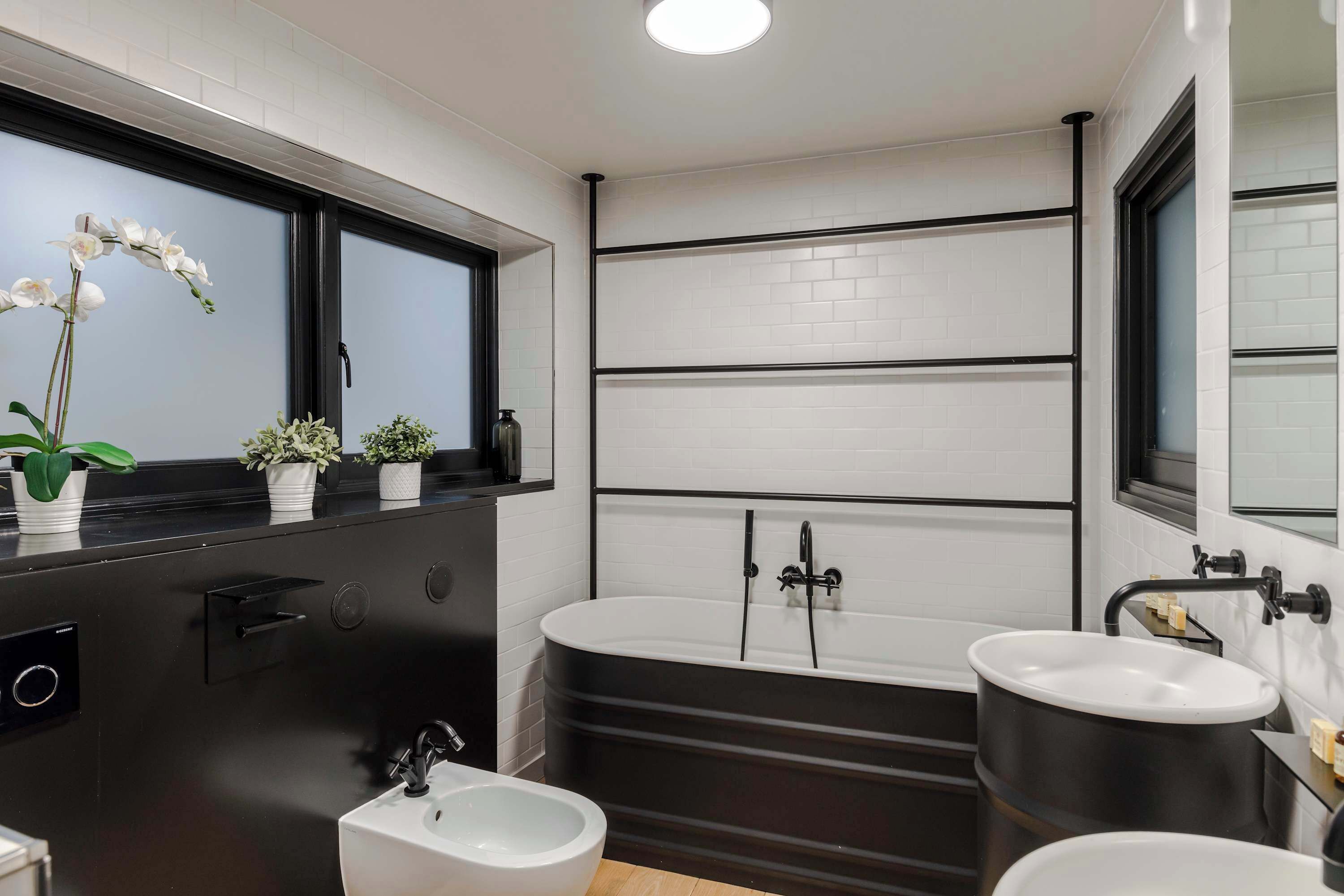 Un baño moderno con tocador negro, lavamanos blanco y bañera.