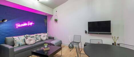 Una sala de estar moderna con sofá, mesa de centro y comedor, que incluye un letrero de neón y un televisor de pantalla plana.