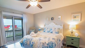 A bedroom with a bed, a nightstand, a ceiling fan, and a view of the ocean through a sliding door. - Welcome to the “Pot O’ Gold” at the end of the rainbow! (St. George Island)