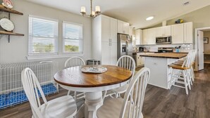 A modern kitchen with white cabinets, a central island, and a dining area with a round table and white chairs. - Welcome to the “Pot O’ Gold” at the end of the rainbow! (St. George Island)
