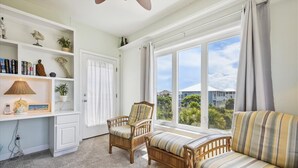 A living room with a large window, wicker furniture, and a bookshelf.