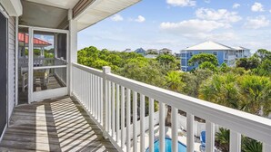 A wooden deck with a white railing overlooking a swimming pool and lush greenery.