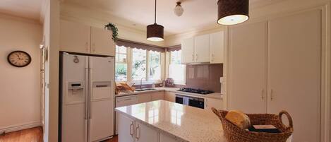 Une cuisine moderne avec des meubles blancs, un plan de travail en granit, une cuisinière encastrée et un luminaire suspendu.
