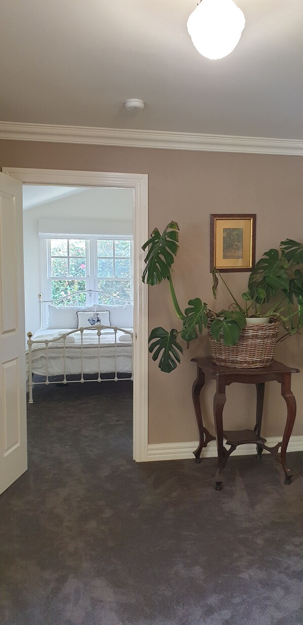 A bedroom with a bed, a window, a potted plant, and a framed picture on the wall.