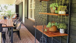 Un patio al aire libre con una mesa y sillas de madera, rodeado de muros de ladrillo y plantas en macetas sobre estantes.