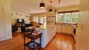 Una cocina amplia con piso de madera, armarios blancos, una isla central e iluminación colgante.