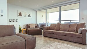 A modern living room with a brown sofa, a matching ottoman, and a large window offering a view. - White Point beach house (Eastbourne)