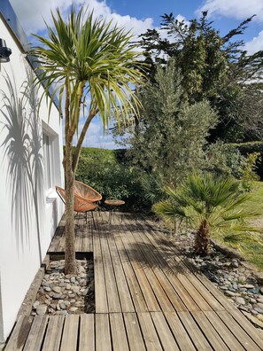 Une terrasse en bois avec un palmier, une chaise et une petite table.