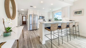 Una cocina moderna con armarios blancos, electrodomésticos de acero inoxidable y una isla central con taburetes.