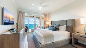 Habitación de hotel con una cama grande, un escritorio, un ventilador de techo y vista al océano.