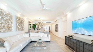 Uma sala de estar moderna com um sofá modular branco, uma mesa de centro de vidro, um console escuro e uma televisão de tela plana grande na parede.