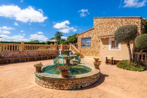 Un patio con una fuente de piedra, plantas en macetas y un edificio de piedra con una ventana.