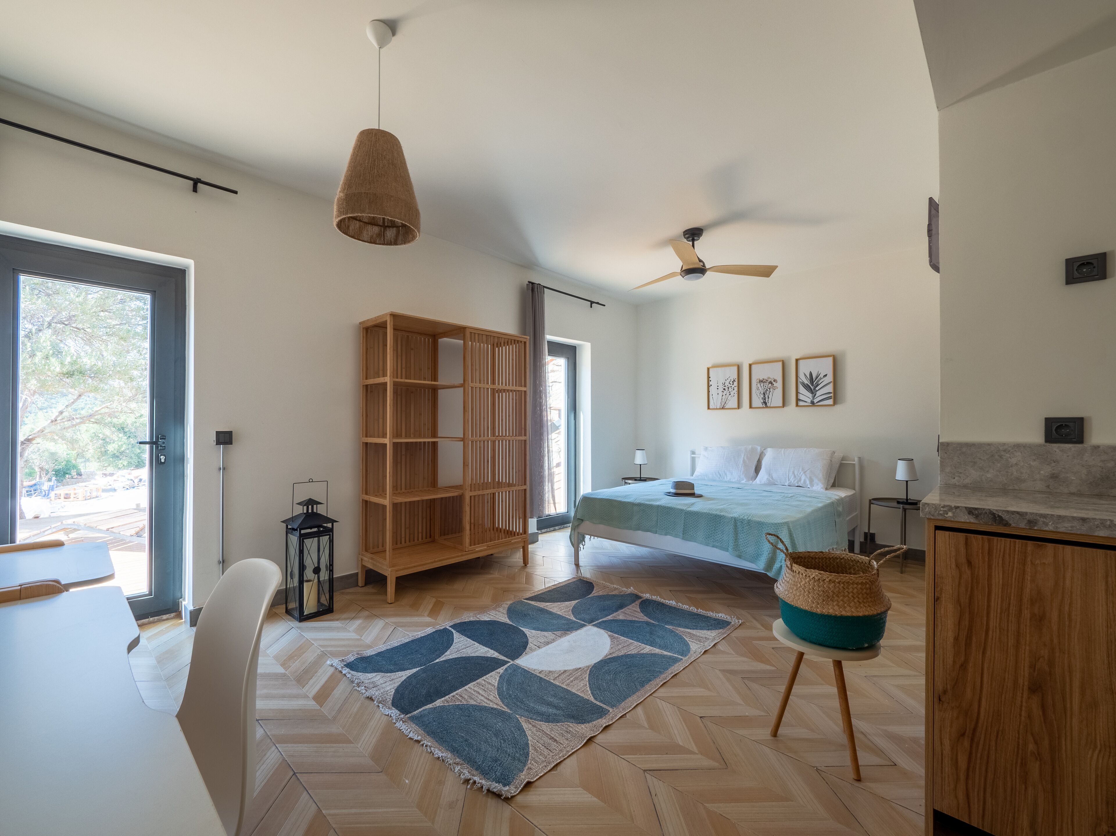 A spacious bedroom with a bed, a ceiling fan, a wooden wardrobe, and a large window.