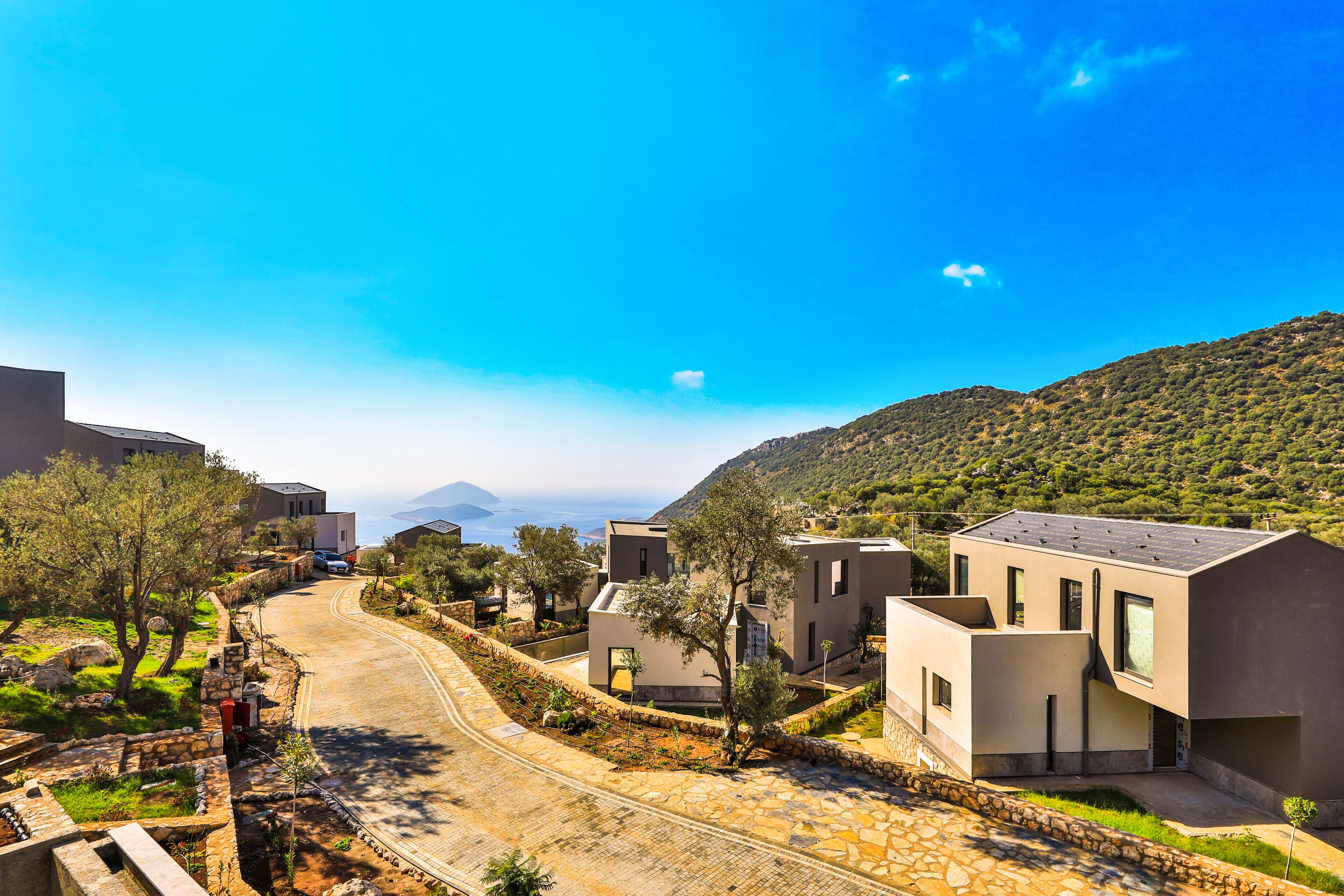 Un quartier résidentiel moderne avec des rues pavées de pierres, des maisons contemporaines et un paysage montagneux en toile de fond.