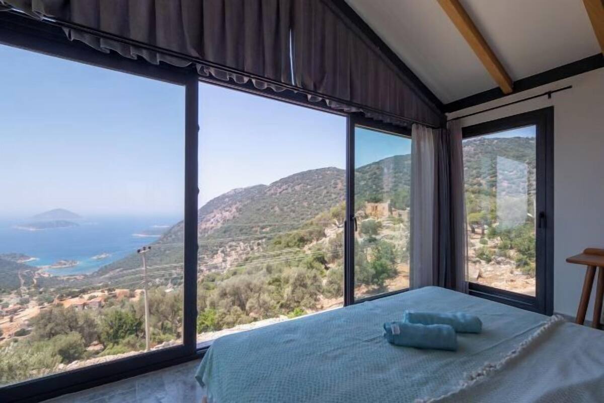 A bedroom with a large window, a bed, and a view of a mountainous landscape.