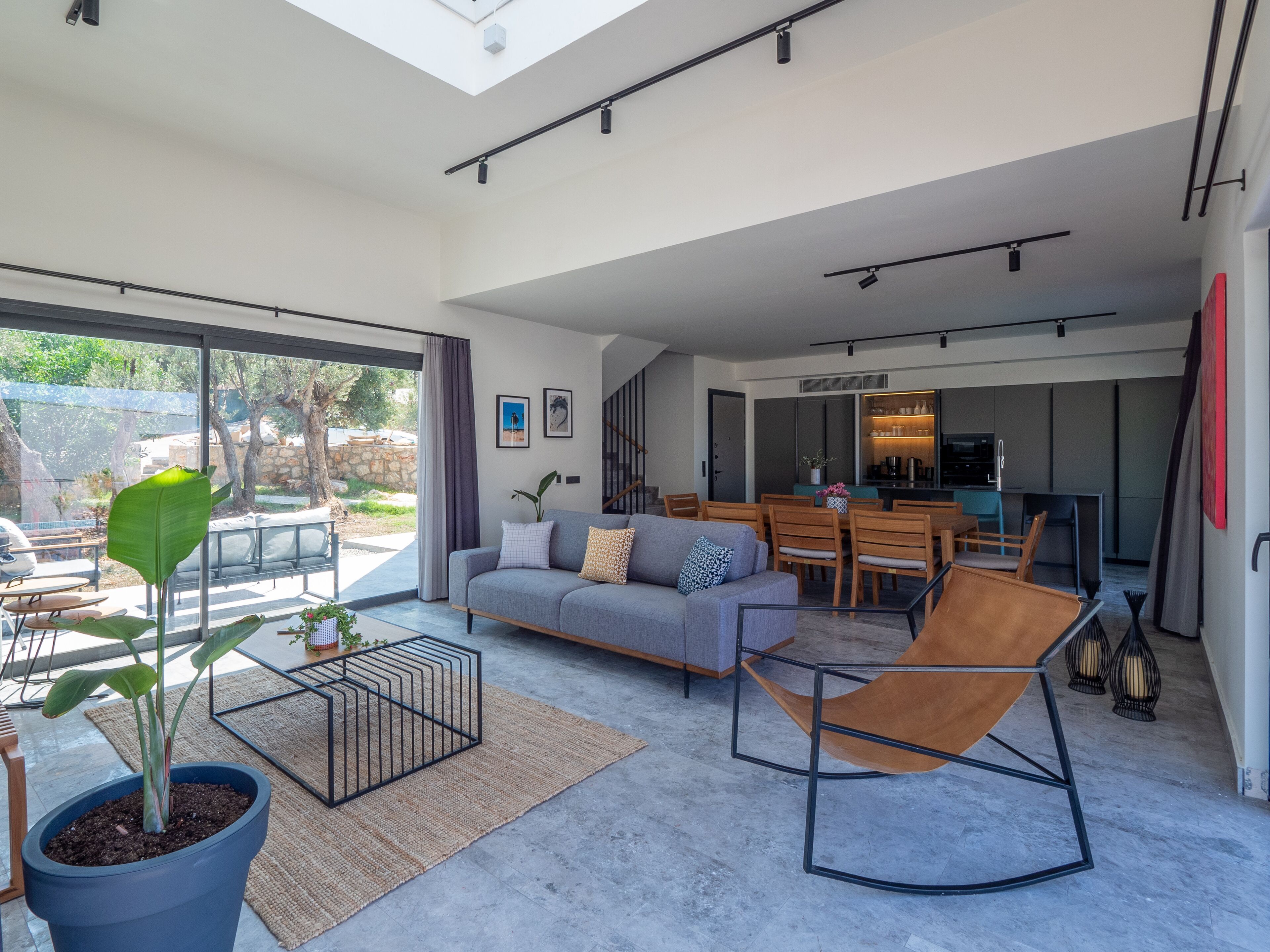 A spacious living area with a sofa, chairs, and a dining table. There is a large window providing natural light and a view of the outdoors.