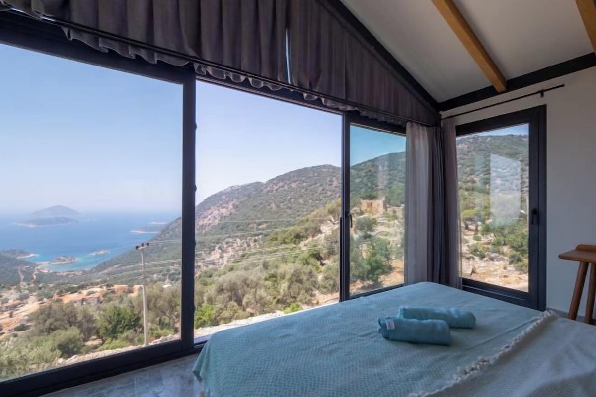 A bedroom with a large window, a bed, and a view of a mountainous landscape.