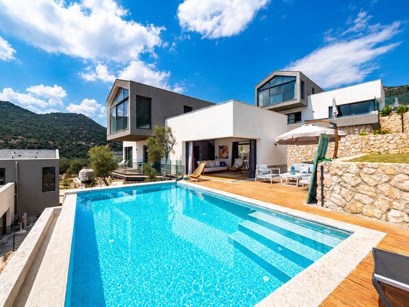 A modern two-story house with a swimming pool, outdoor seating, and a stone wall. - Notos Club (Kas)