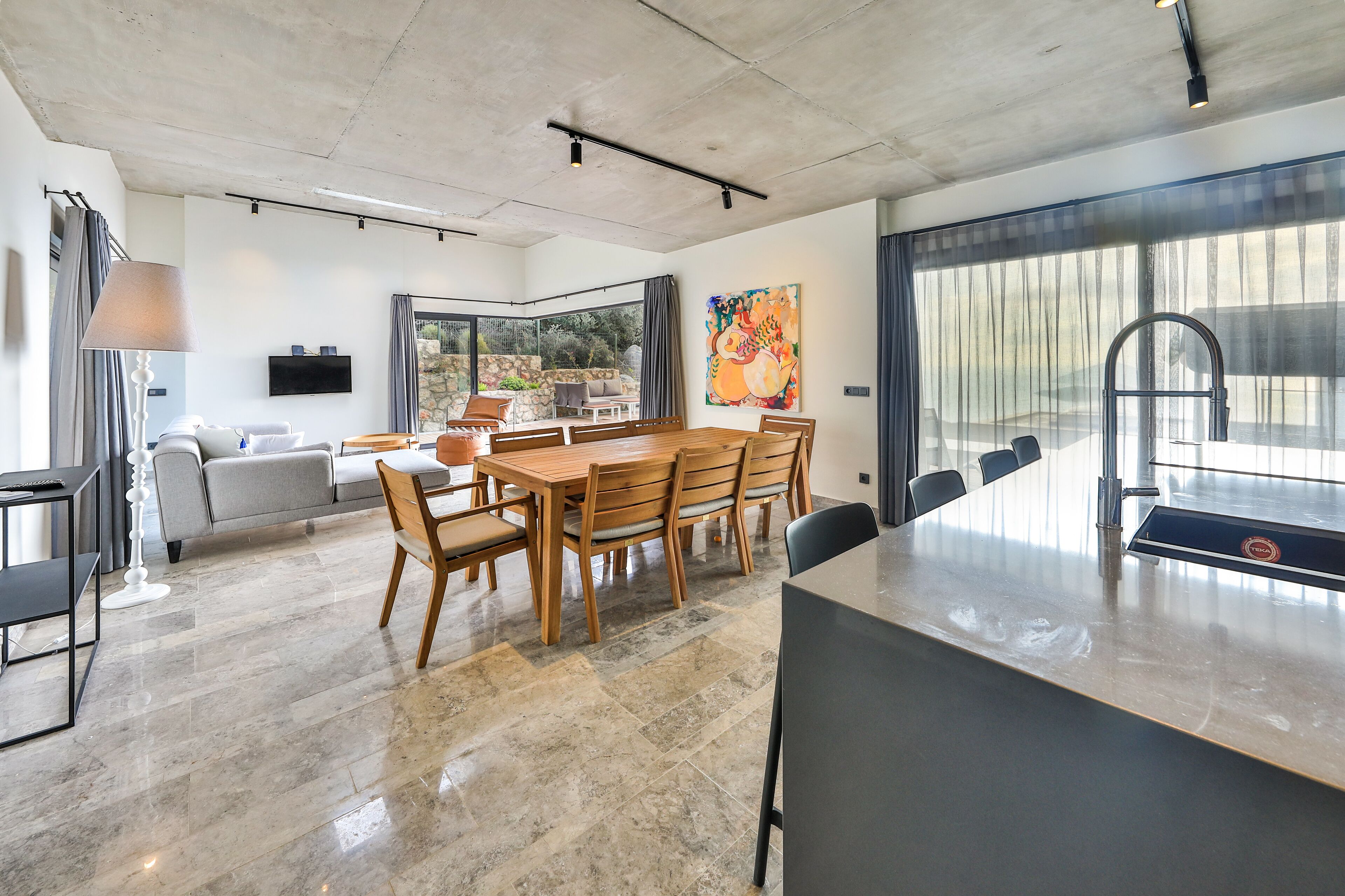 A modern kitchen with a large island, a dining area with wooden chairs, and a view of the outdoors through large windows.
