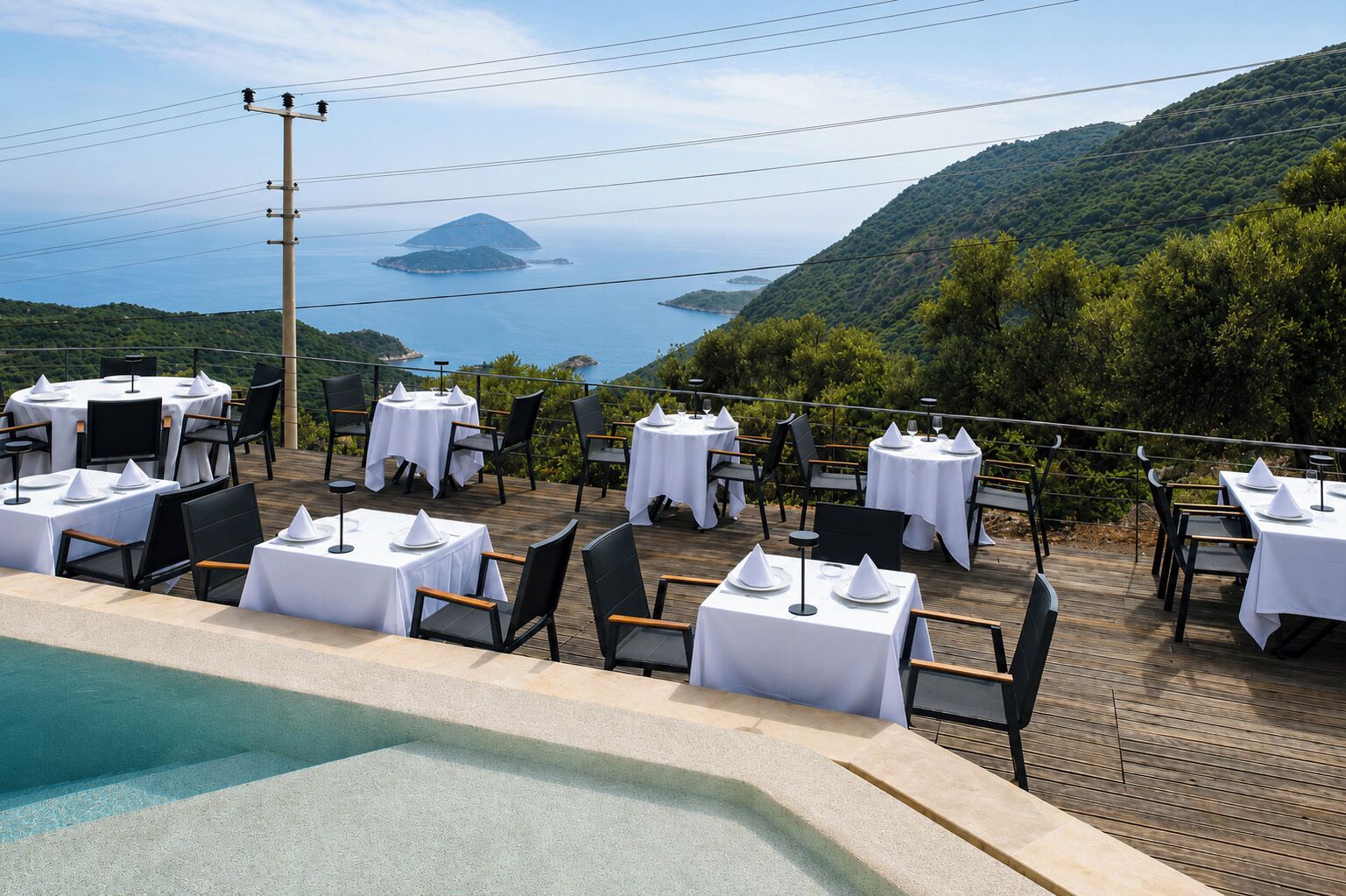 Ein Dachrestaurant mit gedeckten Tischen, das auf eine gebirgige Landschaft und das Meer blickt.