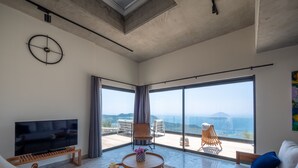 Ein geräumiges Wohnzimmer mit großem Fernseher, einer Couch, einem Couchtisch und einem Balkon mit Blick.