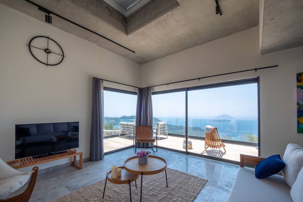 A spacious living room with a large TV, a sofa, a coffee table, and a balcony with a view.