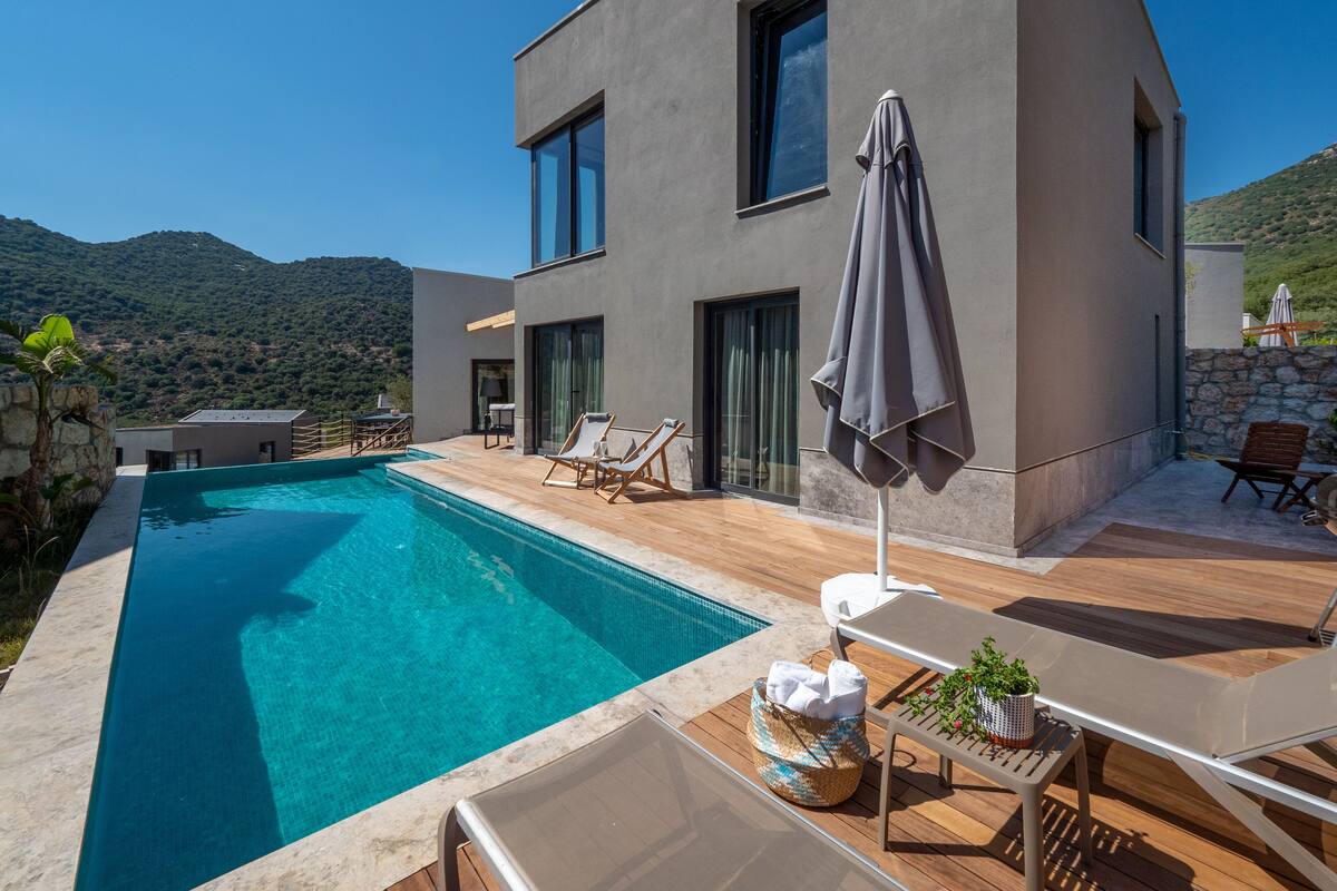A modern villa with a swimming pool, outdoor seating, and a mountain view.