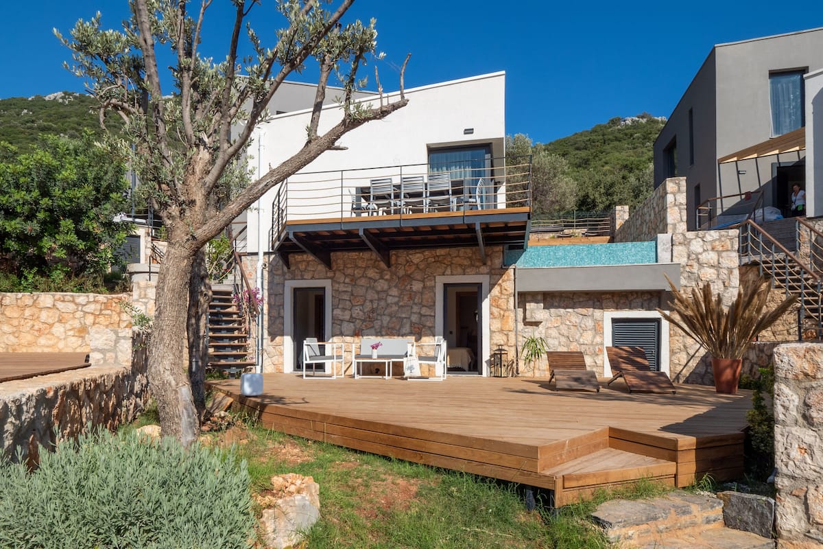 A modern villa with a stone facade, a wooden deck, and outdoor seating.