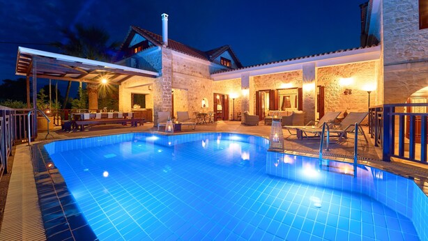 Une piscine avec une terrasse carrelée, un espace extérieur aménagé et couvert, et des murs en pierre.