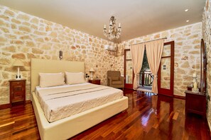 Ein Schlafzimmer mit Steinsandsteinwand, einer Kristallleuchter, einem Bett, einem Sessel und einem Balkon.