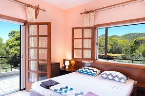 Une chambre à coucher avec un lit, une table de chevet, une fenêtre avec des rideaux et une vue sur la verdure à l’extérieur.