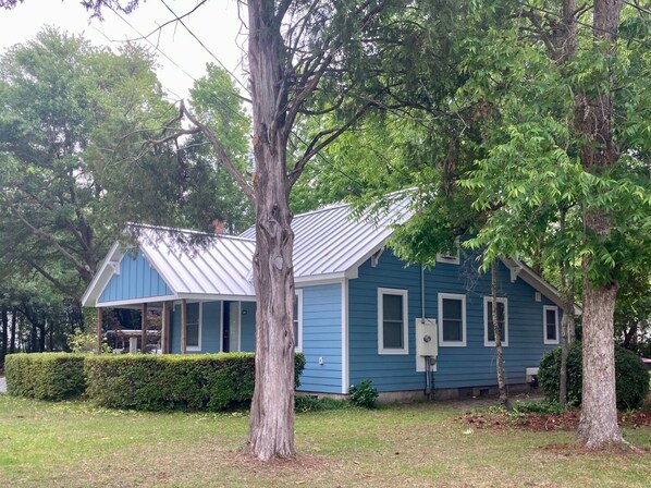 A blue house with a metal roof, surrounded by trees and a hedge. - Cozy Cottage near UNCW, Central Location to All! (Wilmington)