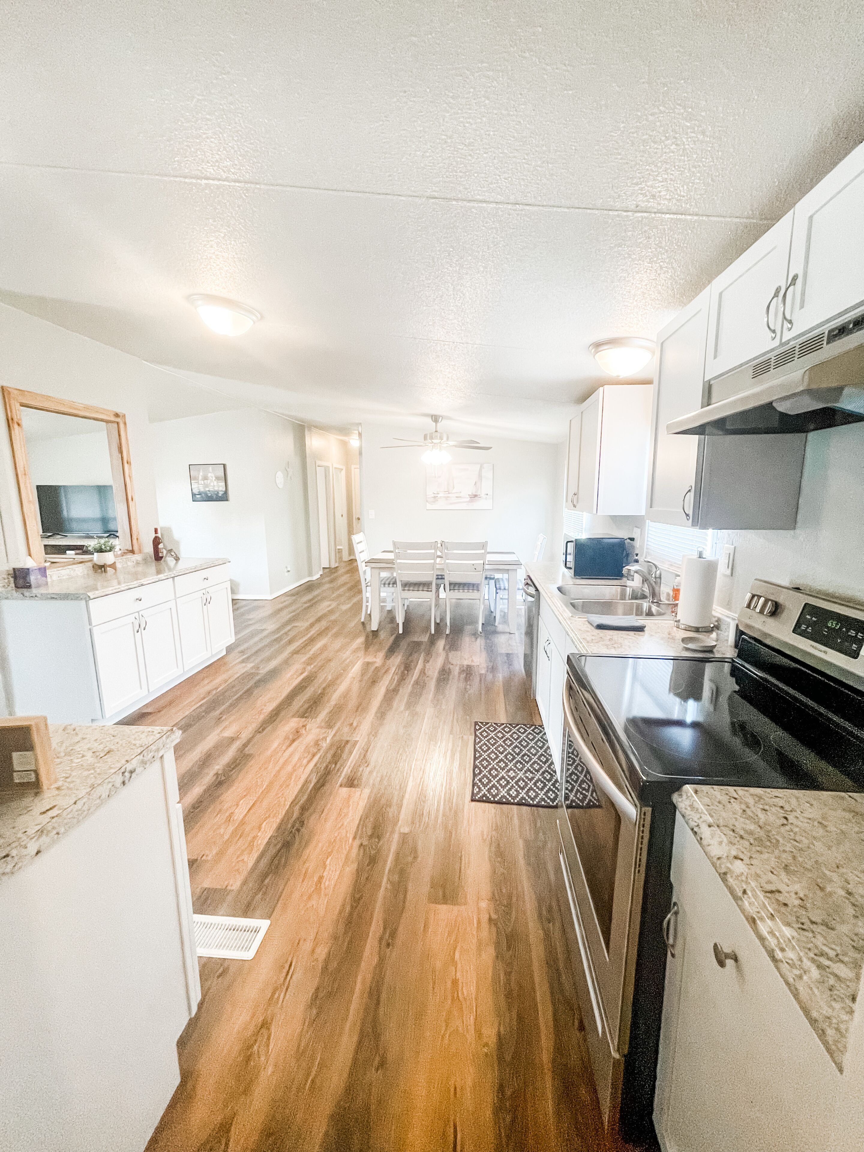 A modern kitchen with white cabinets, a wooden floor, a dining area with a table and chairs, and a microwave.