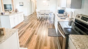 Una cucina moderna con mobili bianchi, pavimento in legno, un'area pranzo con tavolo e sedie e un forno a microonde.