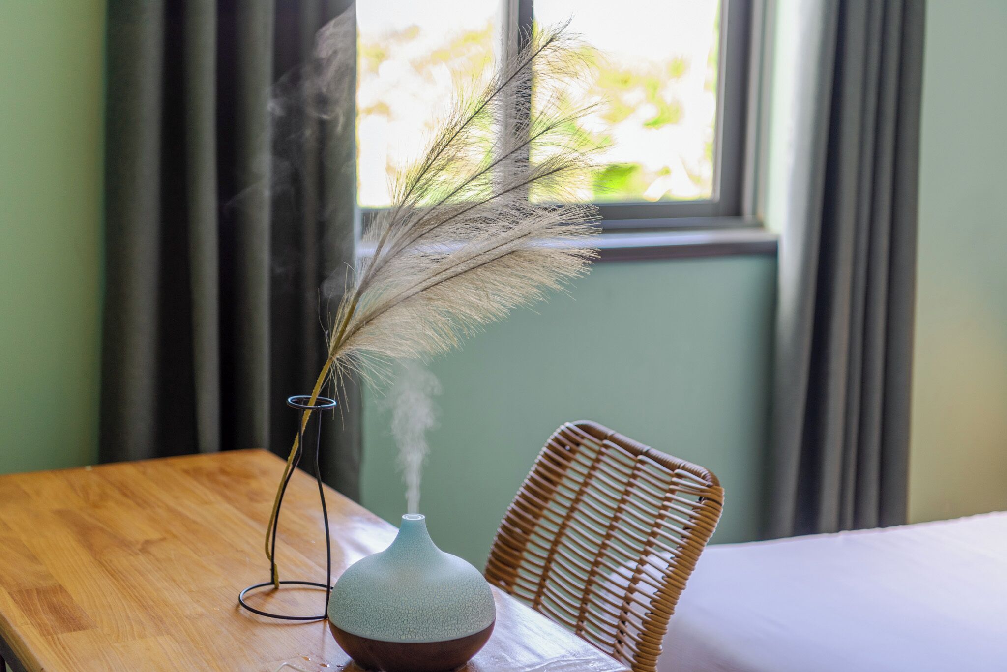 Una mesa de madera con un florero que contiene una planta seca y una silla de mimbre.