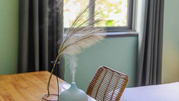 Une table en bois sur laquelle est posé un vase contenant une plante séchée, ainsi qu’une chaise en osier.