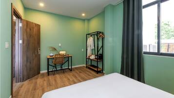 Quarto com cama, escrivaninha, cadeira, cabideiro e janela com cortinas.