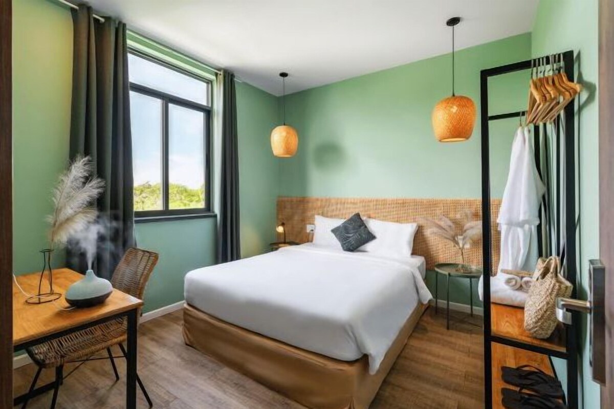 Habitación de hotel con una cama grande, un escritorio con silla, una lámpara colgante y vistas a zonas verdes.