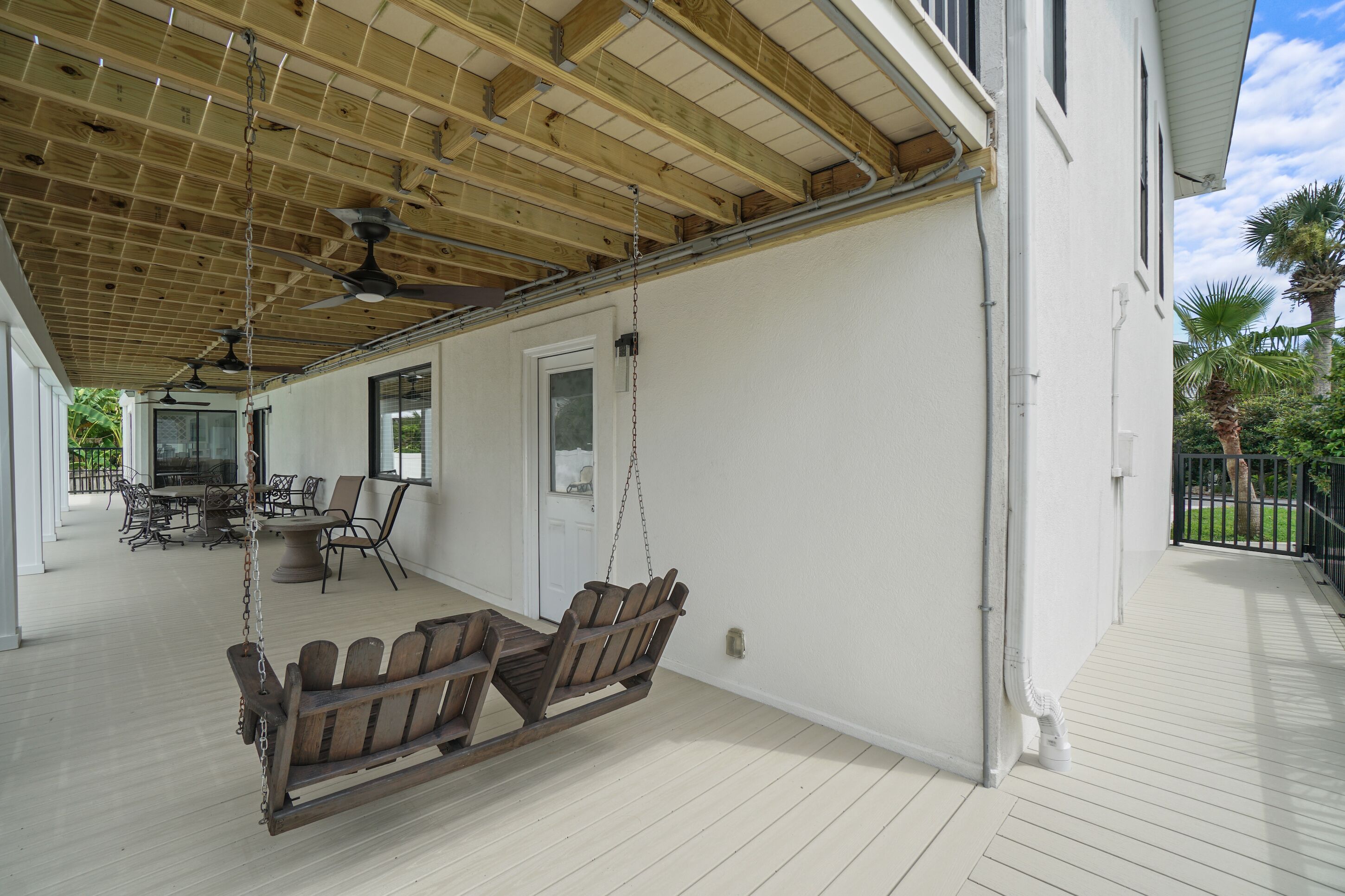 A covered porch with a swing set, a dining table with chairs, and a view of the house's exterior.
