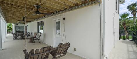 A covered porch with a swing set, a dining table with chairs, and a view of the house's exterior.