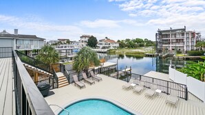 A poolside area with lounge chairs, a pool, and a view of a river and buildings.