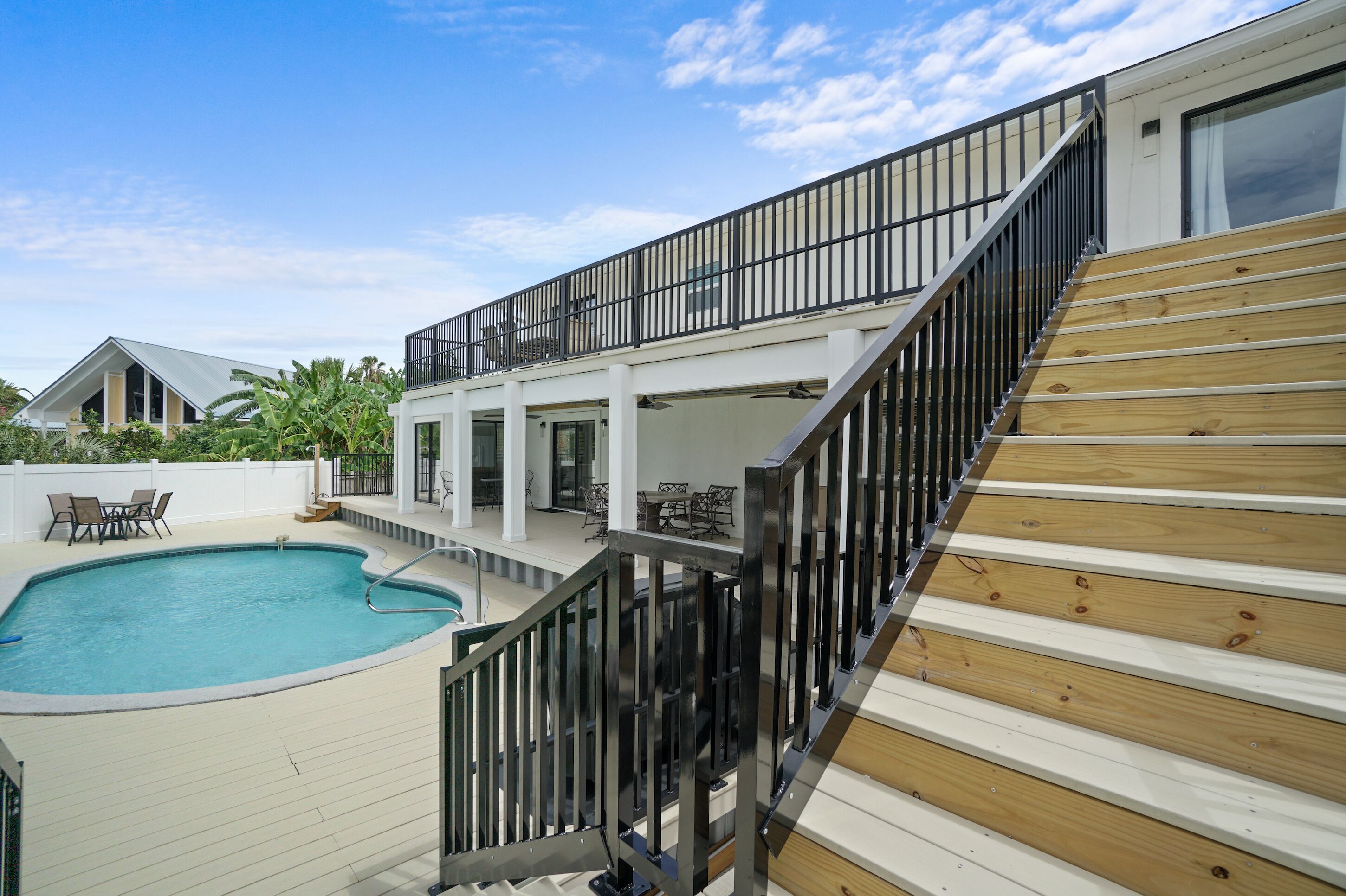 A residential property with a swimming pool, wooden deck, and a balcony with black railings.