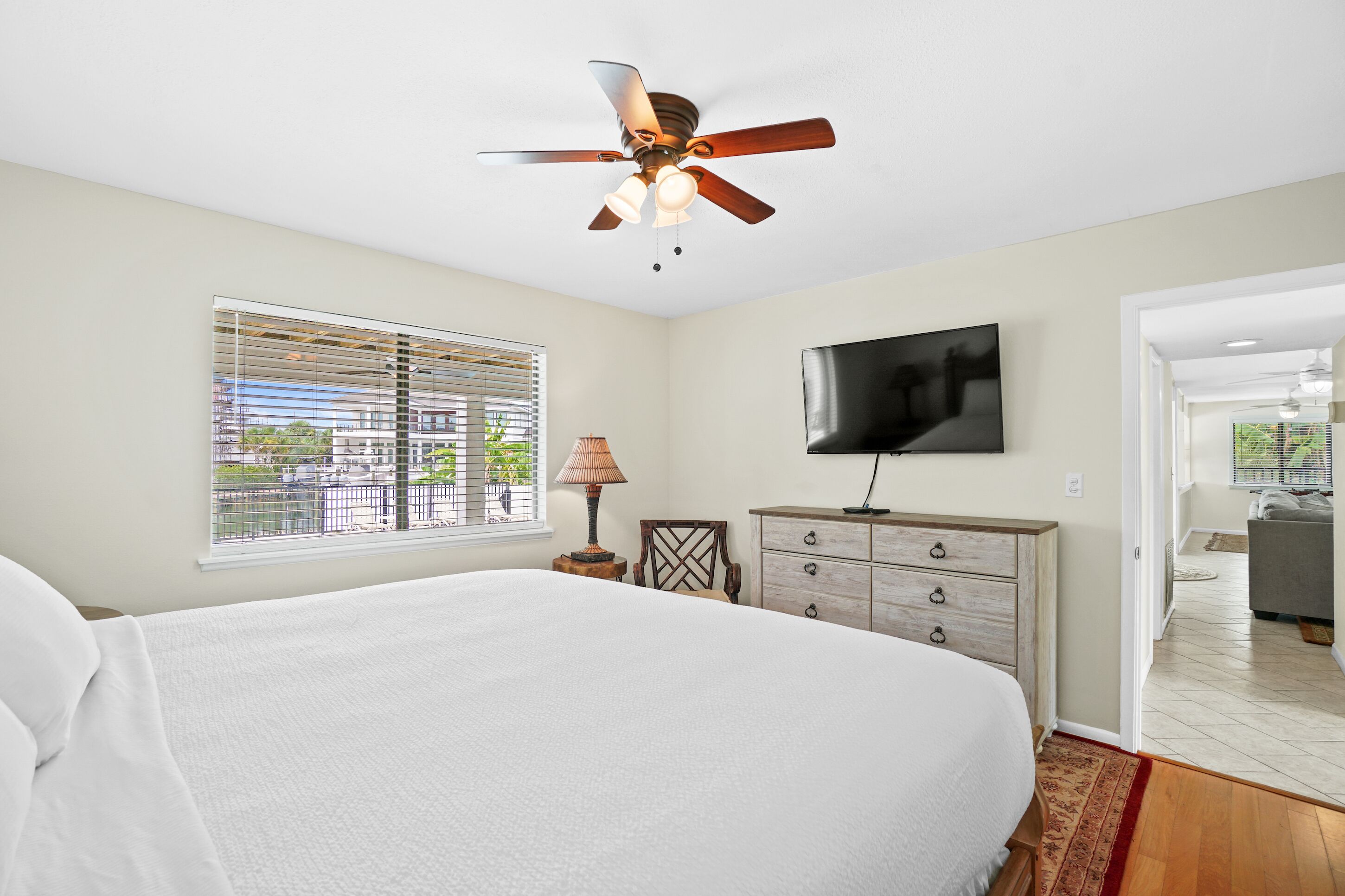 A bedroom with a bed, a ceiling fan, a TV, a window with blinds, and a dresser.